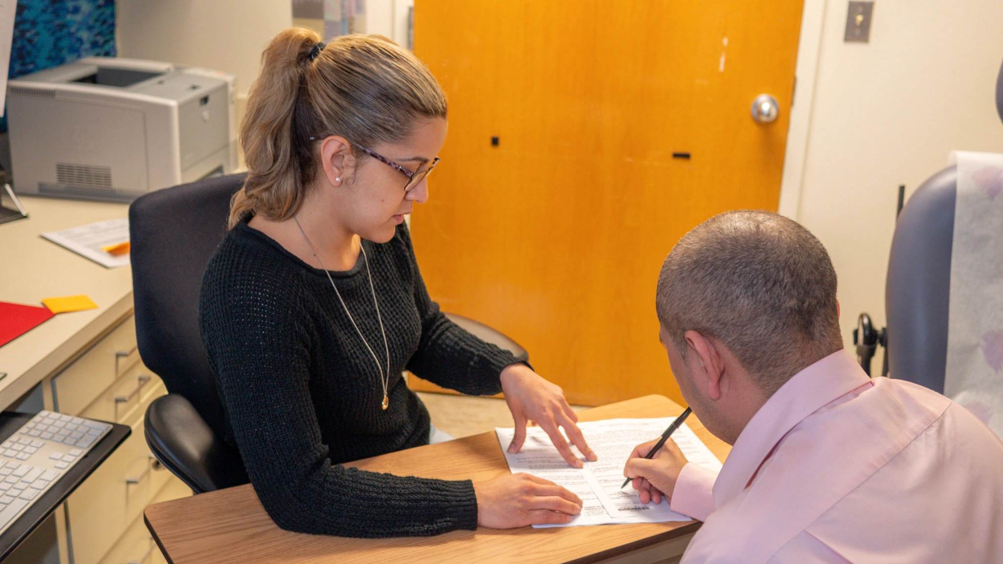 An NIAID clinical-trial volunteer signs an informed-consent form while a staff member points to the study paperwork.
