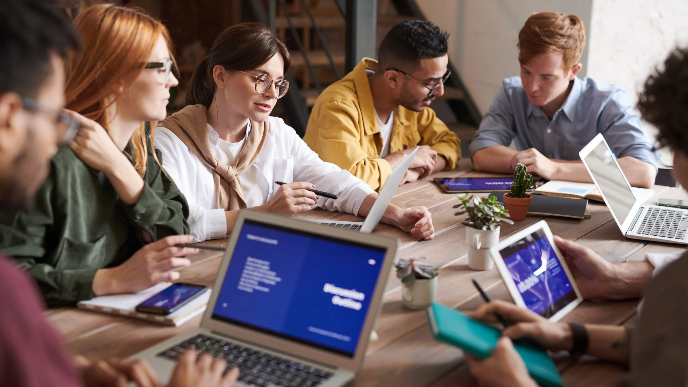 Colleagues review information on laptops and tablets around a shared table during a business discussion.